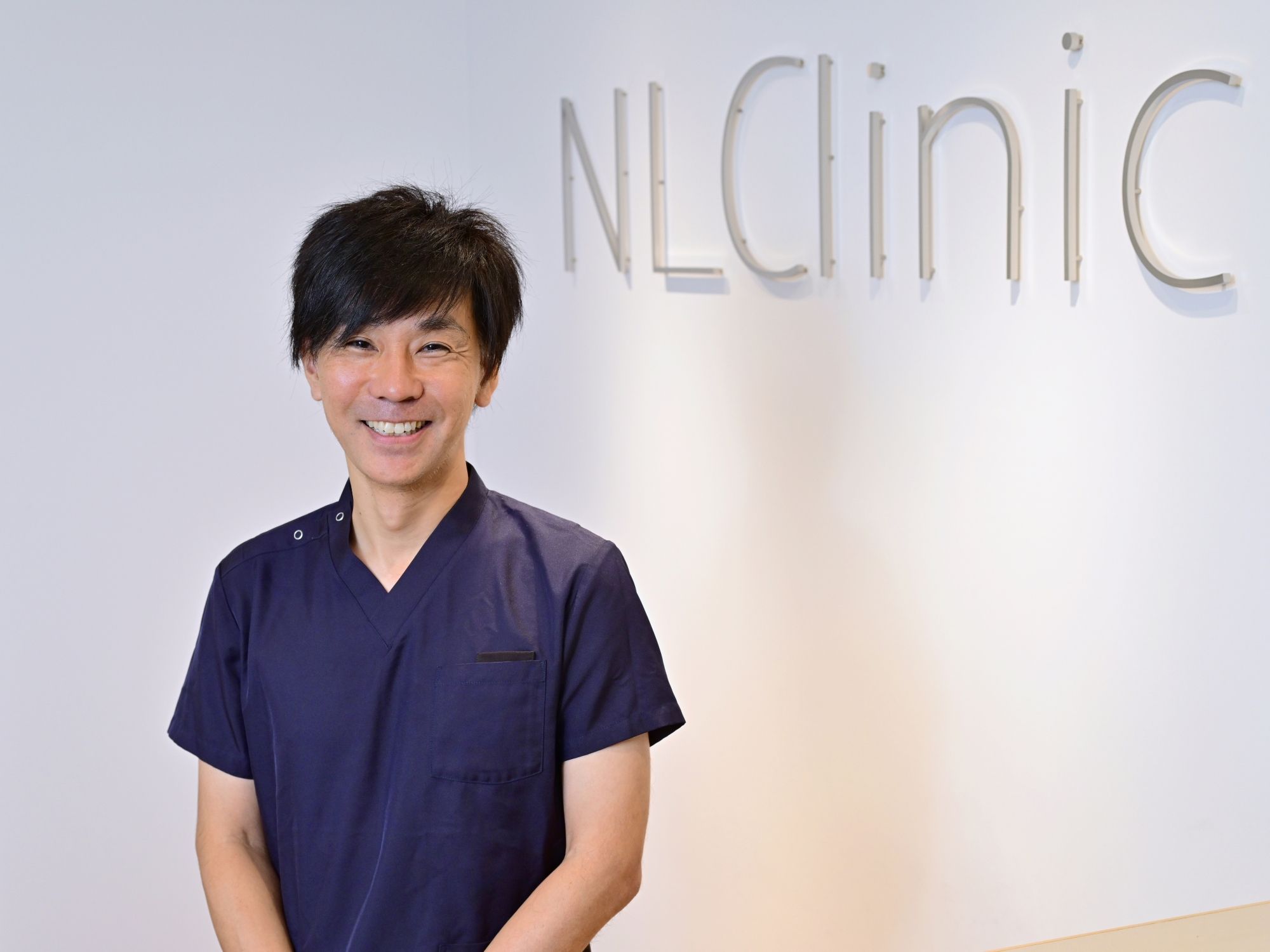 NLC野中腰痛クリニックのロゴの前に立つ野中院長
