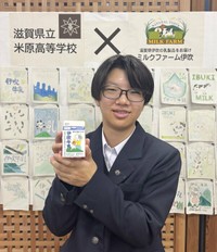 自身がデザインした「伊吹牛乳」のパッケージを手にする米原高の穐元さん。後ろの絵は他の生徒が描いたもの（大津市・滋賀県庁）