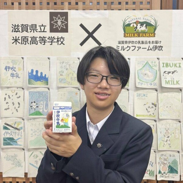 自身がデザインした「伊吹牛乳」のパッケージを手にする米原高の穐元さん。後ろの絵は他の生徒が描いたもの（大津市・滋賀県庁）