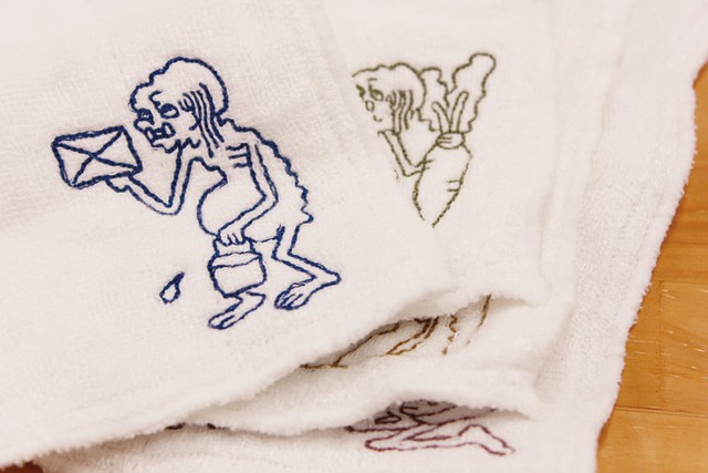 「拭き掃除をする餓鬼」など、白地のふきん右下部分にワンポイント、キャラクターが刺繍されています（提供写真）