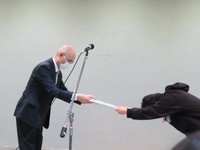 区長から委嘱状を受け取り深々と頭を下げるフィッシャーズ・シルクロード