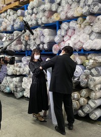 倉庫で生地を見る西側氏（左）＝提供写真