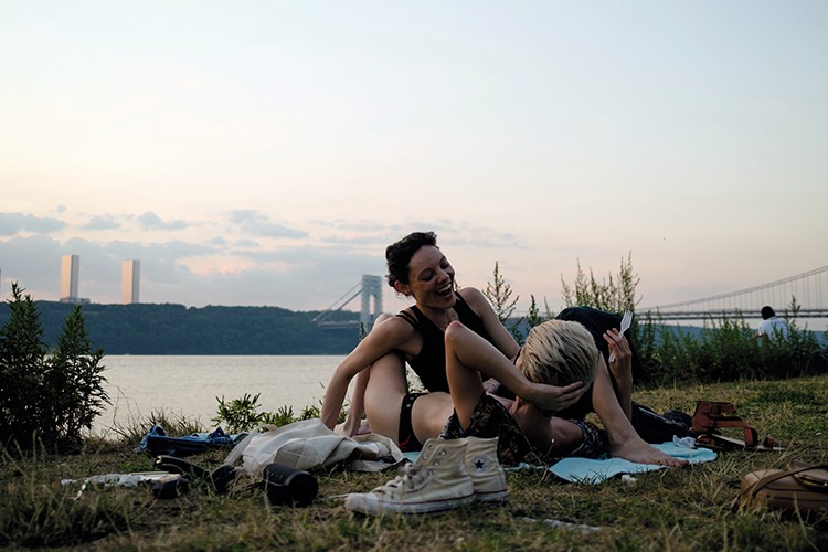 Masha Mikhaylenko and Sara Pasik join crowds along the Hudson River at sunset in New York on July 20, 2022. Water bottles, with sweating beads of condensation, water guns, spraying in parks and inside apartments and fire hydrants transforming into sprinklers. These are some of the tools New Yorkers are using to work and play during the summer's first heat wave, as daily temperatures near 100 degrees. (Jose A. Alvarado Jr./The New York Times)