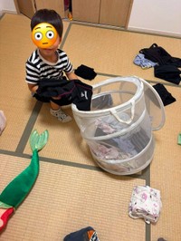 洗濯物かごの前で服をたたむ男の子（まゆこさん提供）