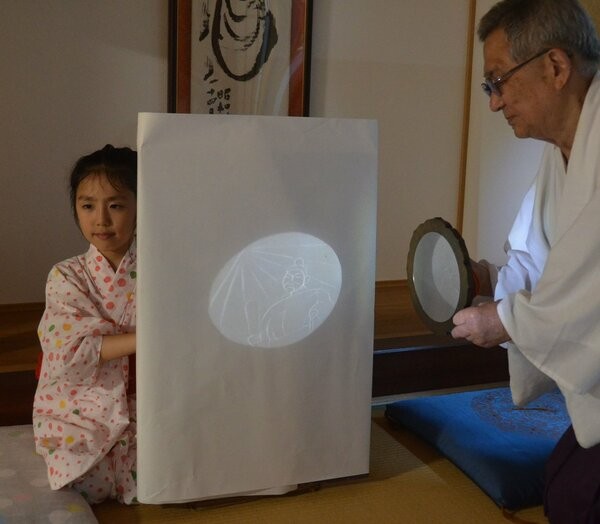 中村宮司が手にした魔鏡に光を当てると、平清盛の像が映し出された
