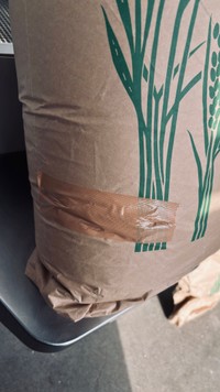 シートベルトの受け口が刺さって破れ、テープで補修された米袋／むちことこつぶさん（@muchi.photo）提供