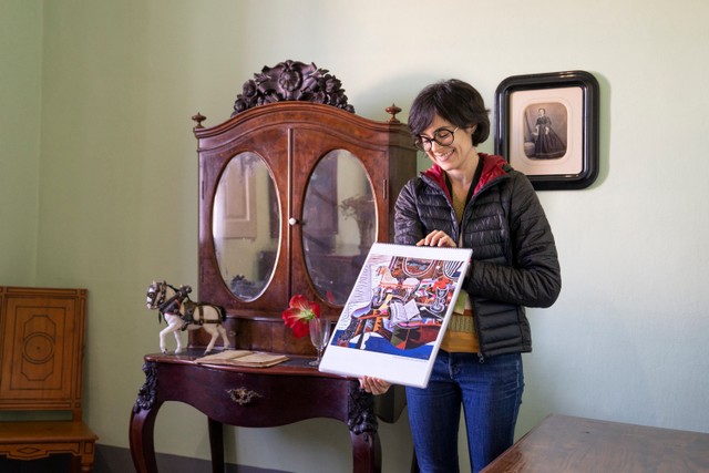 別荘にある化粧棚とアイーダさん。この化粧棚をキュビズムやフォービズムの影響を受けて描いたミロの「馬、パイプ、赤い花」（1919年）が印刷されたスケッチブックを持つマス・ミロ財団のアイーダさん