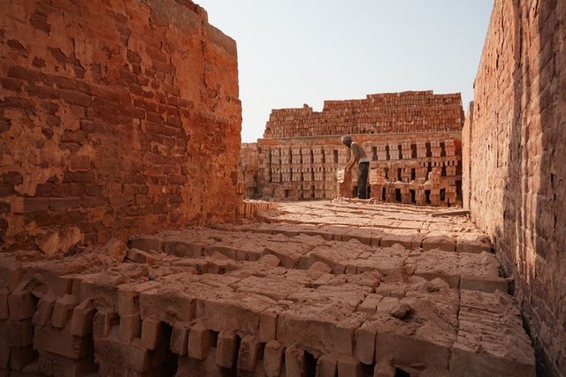 旧式のれんが工場で、赤茶色の粉じんが舞う中、男性が焼き上がったれんがを取り出していた=2024年5月3日、ダッカ郊外、荒ちひろ撮影