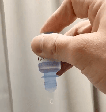 試しに眼科でもらった目薬の底を軽く押すと、ゆっくり一滴出てきた！確かに便利、もっと早く知りたかった。くれぐれも両横を押さないように！（画像提供：ドクターK＠眼科医パパ）