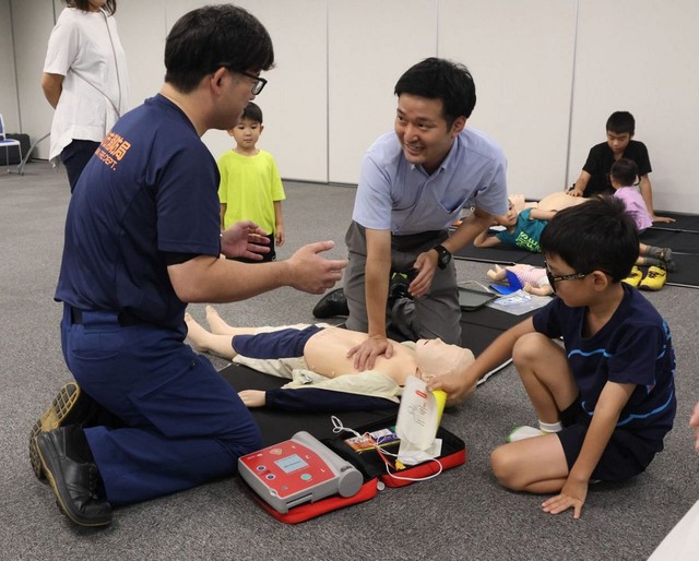 小児救命講習で稲富さん（左）から心肺蘇生の方法を学ぶ記者（中央）＝７月２９日