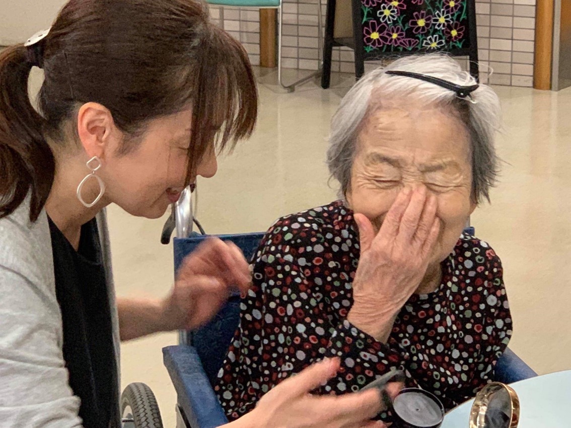 特別養護老人ホームへの出張サービスで、女性に撮影前のメイクをほどこす山田真由美さん（左）