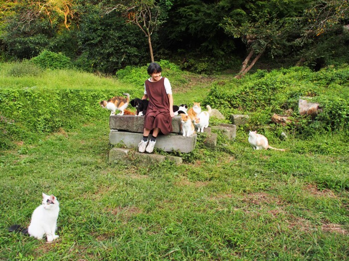 サチがいた里山は、保護した子猫たちが加わりまたにぎやかになった。写真は麻里子さんと猫たち。ゴロー（手前）も今秋旅立ち、今はサチとともに……。（佐竹茉莉子撮影、「猫との約束」より）