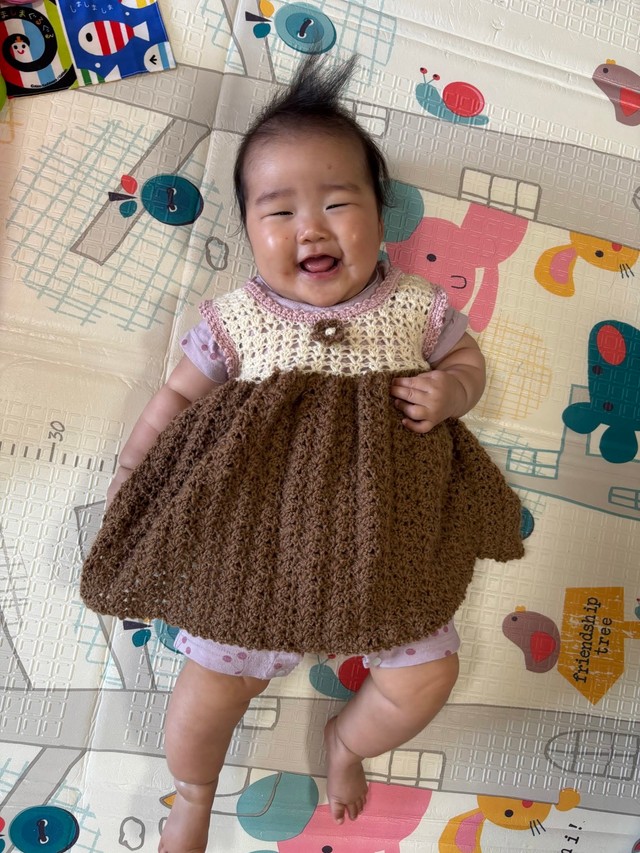 お向かいのおばあちゃんが編んだワンピースを着て、笑顔を見せる生後6カ月の娘／「あーちゃんちゃん」さん（@aydayo221）提供