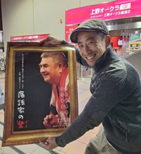 映画「落語家の業」のポスターを手に、映画館を回って営業活動を続ける榎園喬介監督＝東京・上野