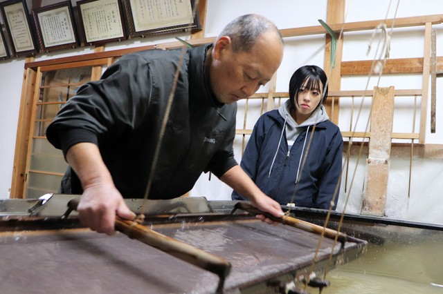 父敏弘さんが紙をすく手つきを見つめる良子さん（福知山市大江町二俣・田中製紙工業所）