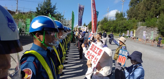 名護市辺野古への新基地建設に抗議してプラカードを掲げる人たちと警備員（提供画像）