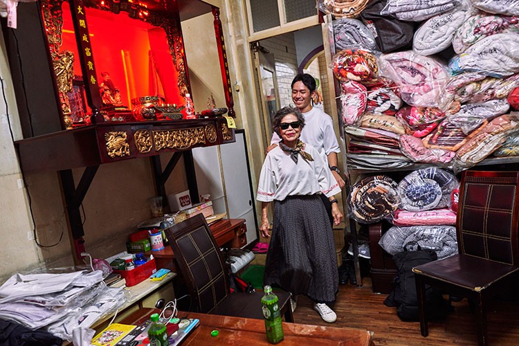 Reef Chang, who dreamed up the Instagram account idea for the laundry business of his grandparents, walks behind his grandmother Hsu Sho-er, who is photo-ready in a new outfit of forgotten clothes, at the shop in Taichung, Taiwan, July 23, 2020. The octogenarian owners of Wansho Laundry in central Taiwan have become Instagram stars for posing in garments left behind. (An Rong Xu/The New York Times)