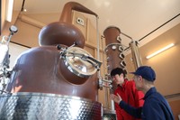 宮下酒造の社員から蒸留の工程について説明を受ける秋山社長（左）＝３月、宮下酒造