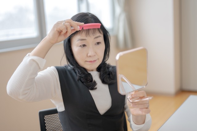 前髪を整える中高年女性　※写真はイメージ（YUTO PHOTOGRAPHER/stock.adobe.com）