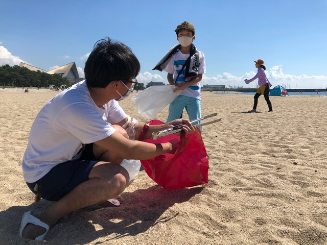青く晴れた空の下、ごみを拾う参加者＝須磨海岸