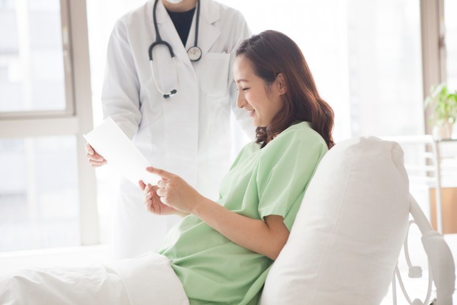 病院のベッドで書面を見る女性※画像はイメージです（Monet/stock.adobe.com）」
