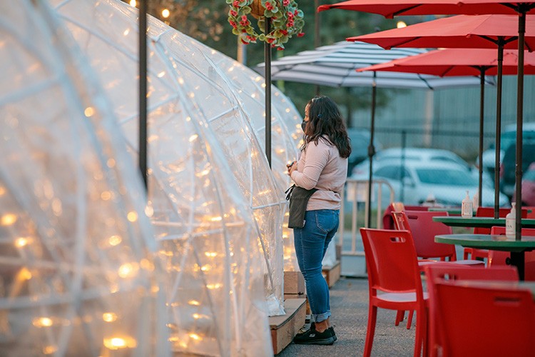 A waitress talks to patrons in one of the plastic igloos that My Brother's Bar has set up outside the establishment to help limit spread of the coronavirus, in Denver, Nov. 6, 2020. Before the pandemic, dive bars were an endangered species in many cities, and some assumed that the coronavirus would make all the great dives descend into dirt. Yet if you think you know that, you don't know dives. (Matthew Staver/The New York Times)